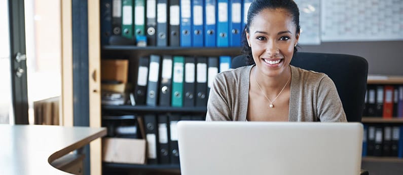 A smiling business professional behind her computer, sitting at a desk. 