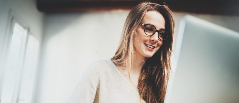 Happy smiling young female student using laptop at library, cheerful hipster girl working on portable computer at vintage loft, attractive businesswoman working via computer at modern office